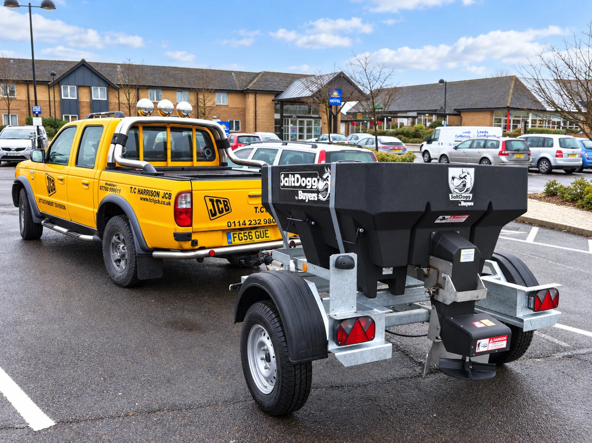 SaltDogg hopper spreader on a trailer behind a yellow pickup