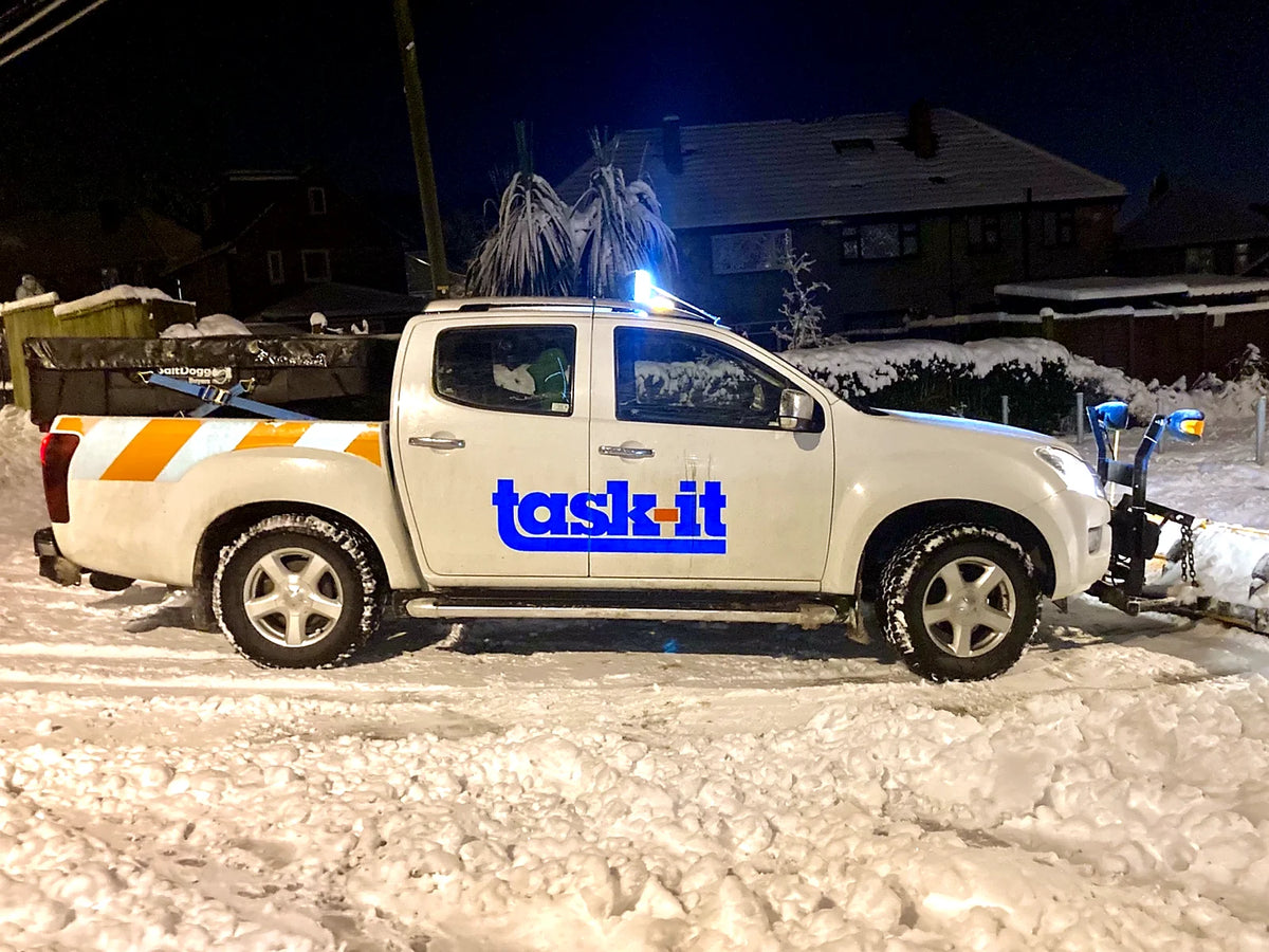White service pickup fitted with a SaltDogg SHPE0750 hopper spreader in a snowy yard at night